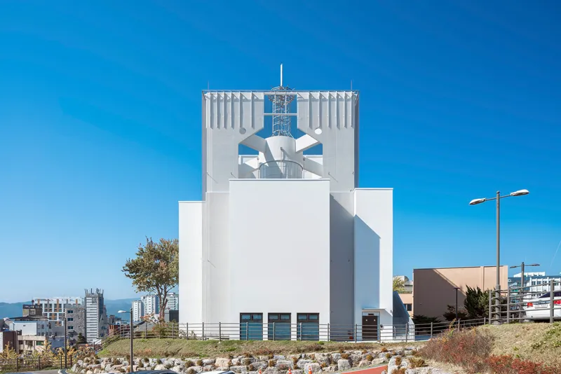 White facade with vertical corrugation and perforated upper section featuring geometric cutouts against a blue sky