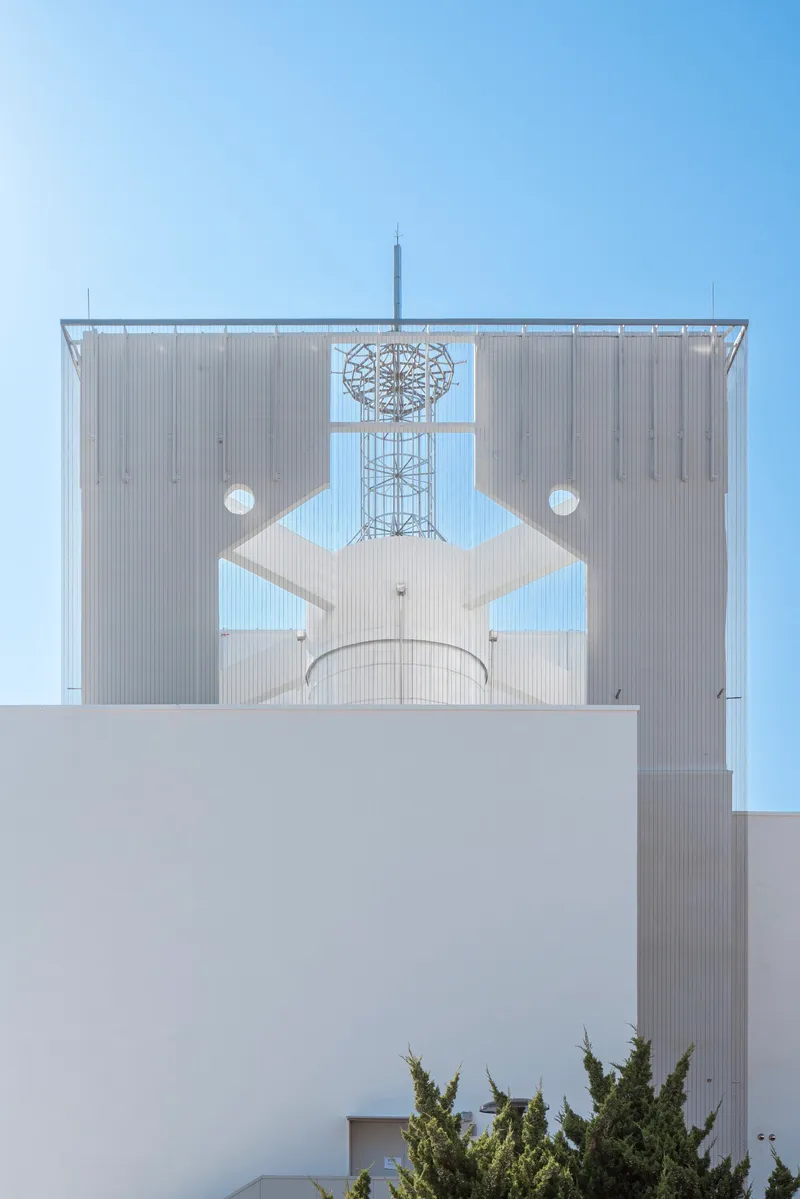 Metal screen facade with geometric cutouts framing a communications tower against clear blue sky