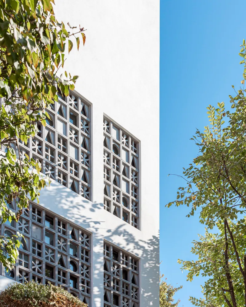 Corner view of geometric window screens on white facade with trees framing left and right