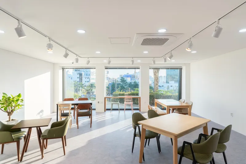 Interior dining room with timber tables, olive upholstered chairs, and floor-to-ceiling windows overlooking greenery