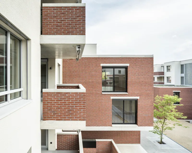 Stacked brick balconies with metal railings and offset volumes facing courtyard with planted tree below