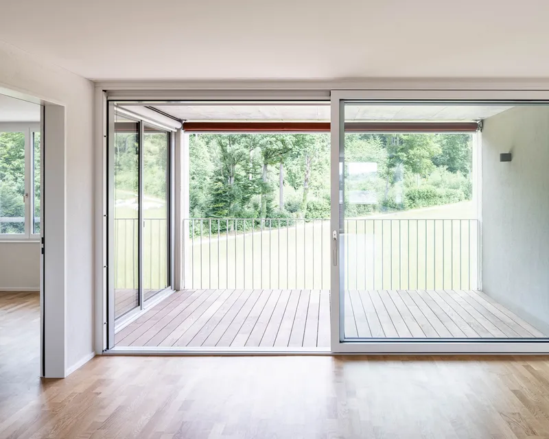 Interior room opening to timber deck balcony with vertical slat railing overlooking green landscape