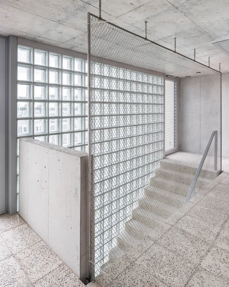 Interior corridor with patterned glass block partition and concrete balustrade beneath an exposed concrete ceiling