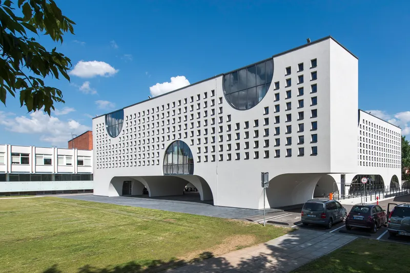 Facade with square window grid and circular glazed openings above rounded arches under a summer sky