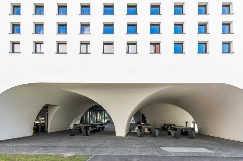 Covered entrance area with three curved archways and black timber benches on paved surface