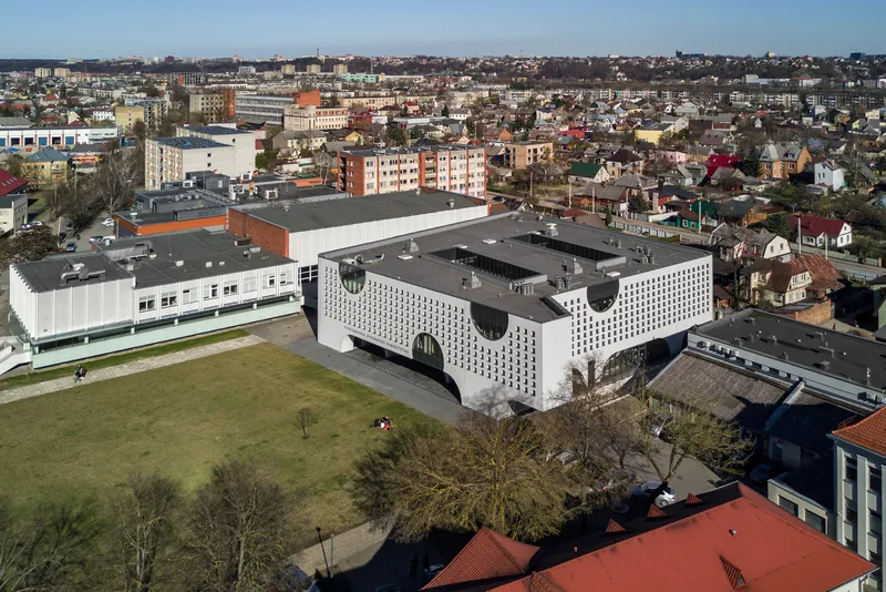 Aerial view of the U-shaped building with perforated facade and circular cutouts in a residential neighborhood