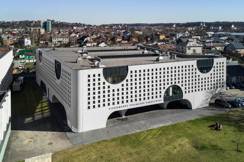 Aerial view of the white perforated facade with circular glazed cutouts and arched ground-level openings