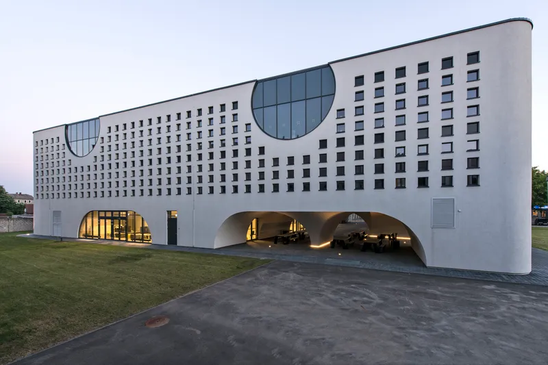 Corner view of the white facade with circular glazed windows and deep arched openings at ground level