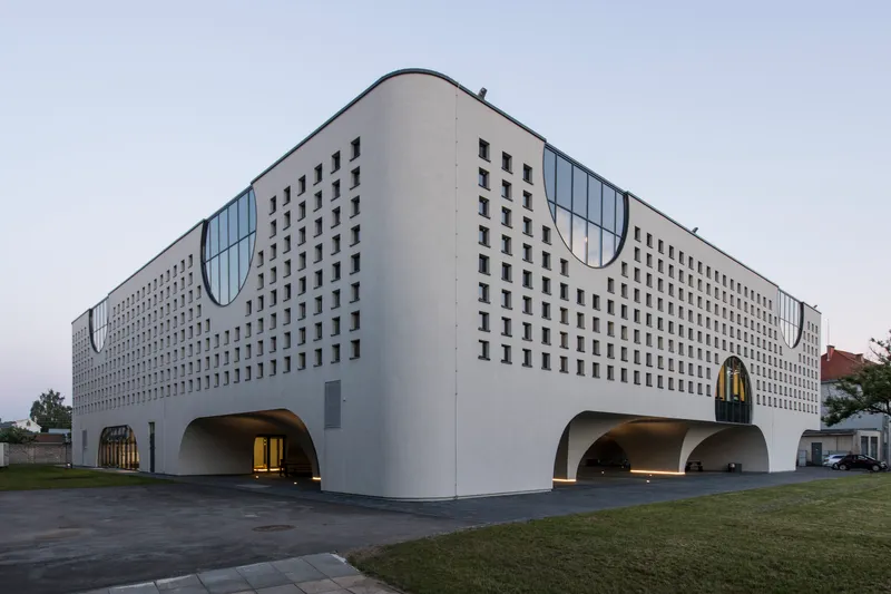 Long facade with repeating square window pattern and curved roofline under overcast evening sky