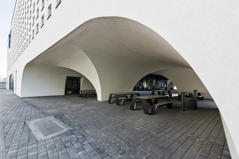 Covered terrace beneath vaulted white arches with dark timber benches on grey pavers