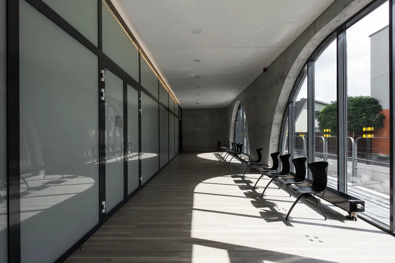 Glazed corridor with black metal frames along concrete wall and afternoon light on timber flooring