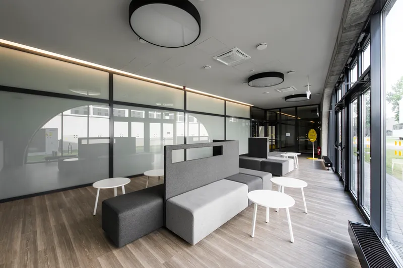 Open lounge area with grey fabric seating modules and frosted glass partition under linear ceiling lighting