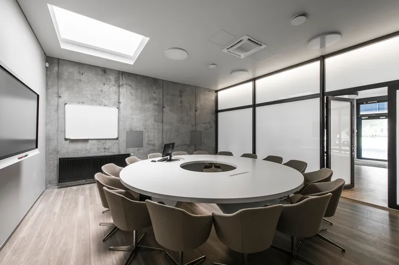 Conference room with circular table beneath a skylight and exposed concrete wall with whiteboard