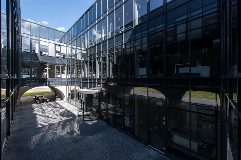 Courtyard terrace with black glass facades reflecting arched openings under blue sky