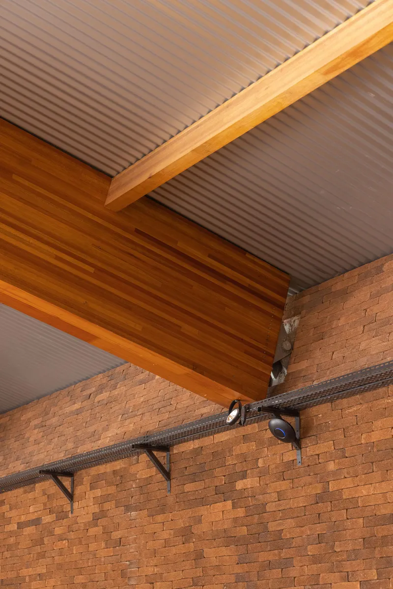 Detail of the timber beam junction with corrugated metal ceiling and exposed brick wall below