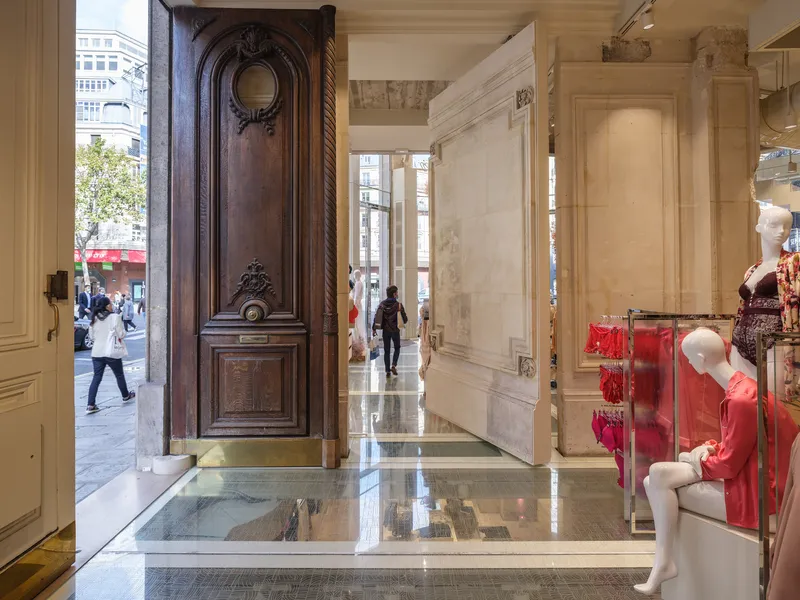 View through carved timber entrance doors toward glass floor panels revealing the basement level below