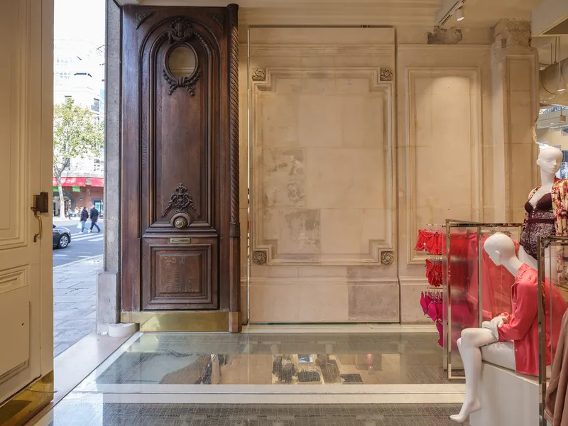Ornate timber door propped open with stone paneled walls and glass floor revealing lower level
