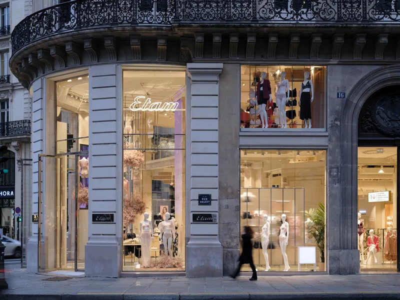 Ground level storefront facade with tall display windows and wrought iron balcony above at twilight