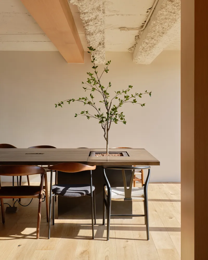 Dining table with integrated planter and branch centerpiece beneath exposed concrete ceiling