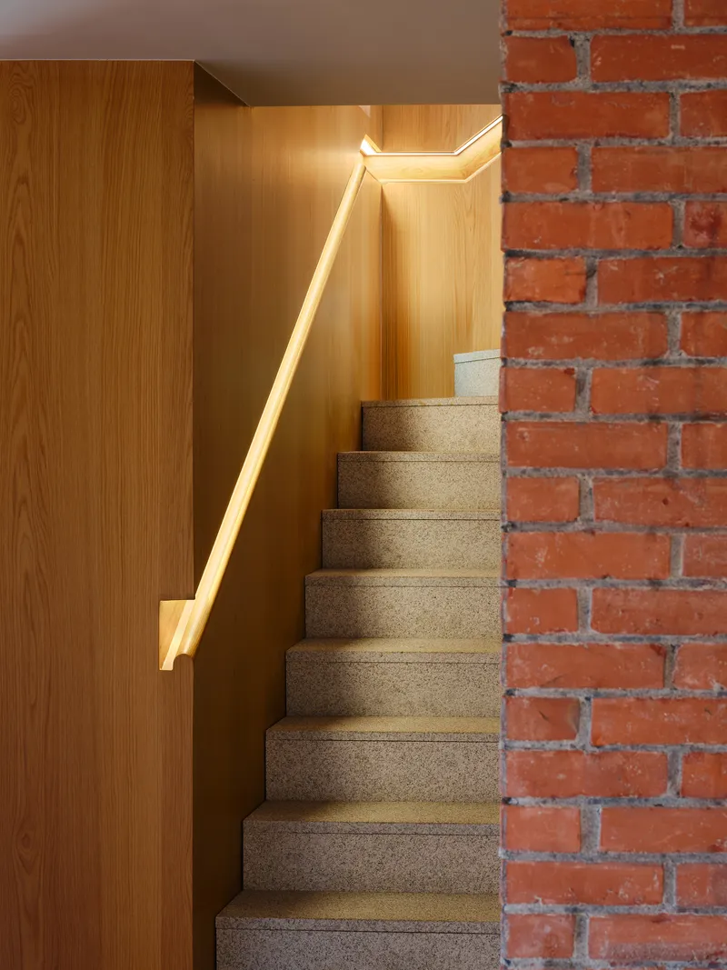 Terrazzo staircase with integrated handrail lighting alongside exposed brick wall