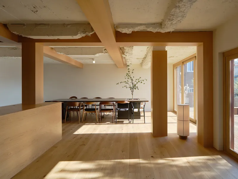 Open-plan interior with timber columns framing a dining area and exposed concrete ceiling beams in afternoon light