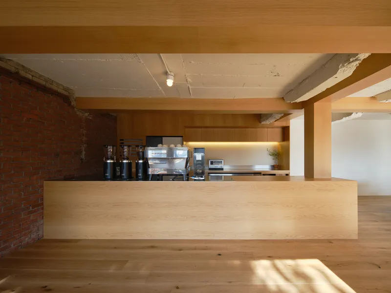 Light wood service counter against exposed brick wall with integrated kitchen beneath a concrete ceiling