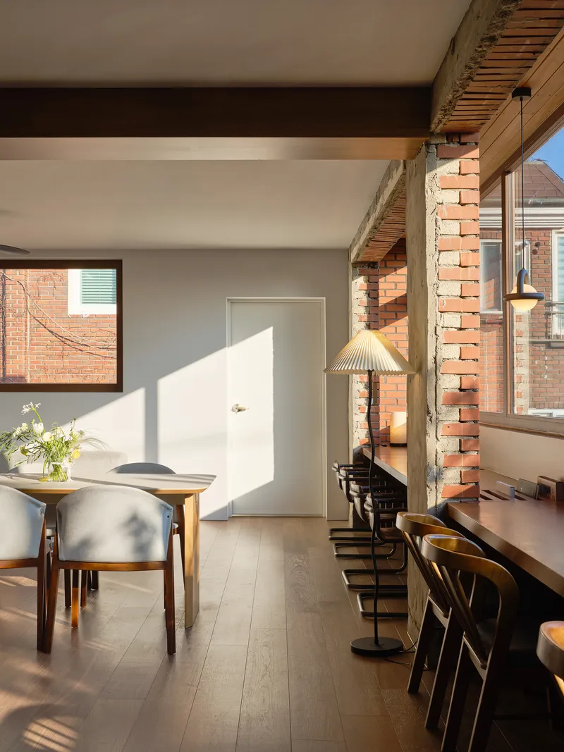 Dining area with exposed brick column and timber beams casting strong shadows across the white door