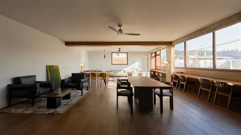 Open plan living and dining area with exposed brick wall and ribbon windows overlooking rooftops