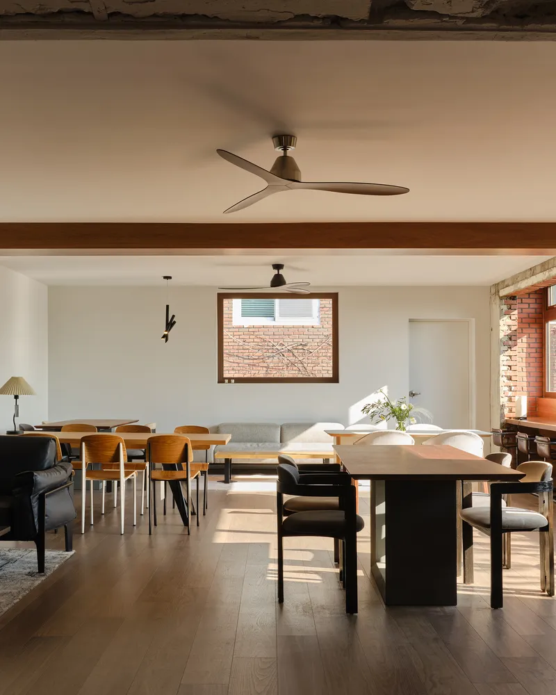 Living and dining space with horizontal timber trim beneath exposed brick wall framing a window