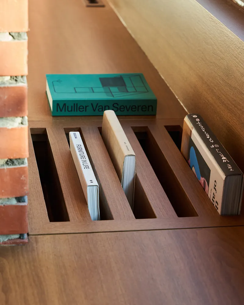 Custom timber shelf with slotted compartments holding books beside a brick wall