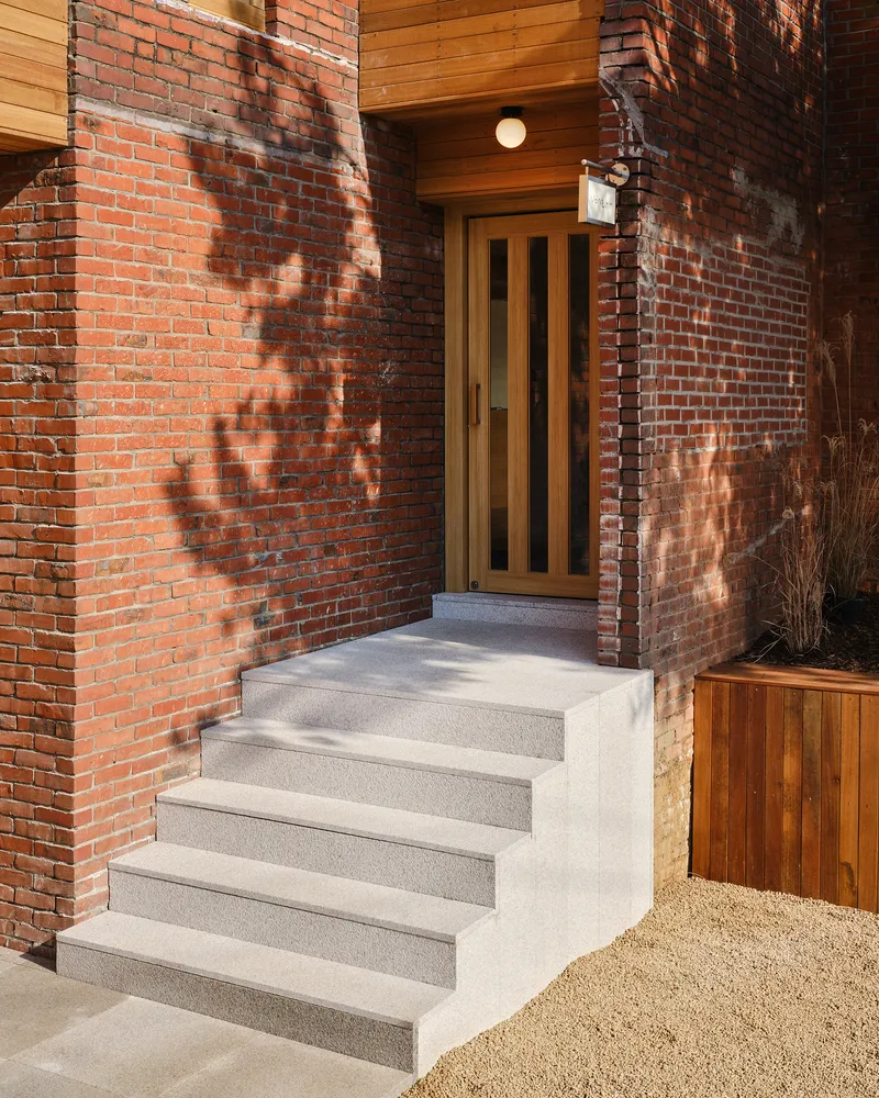 Exterior entry stair in poured concrete against weathered red brick wall in afternoon sunlight