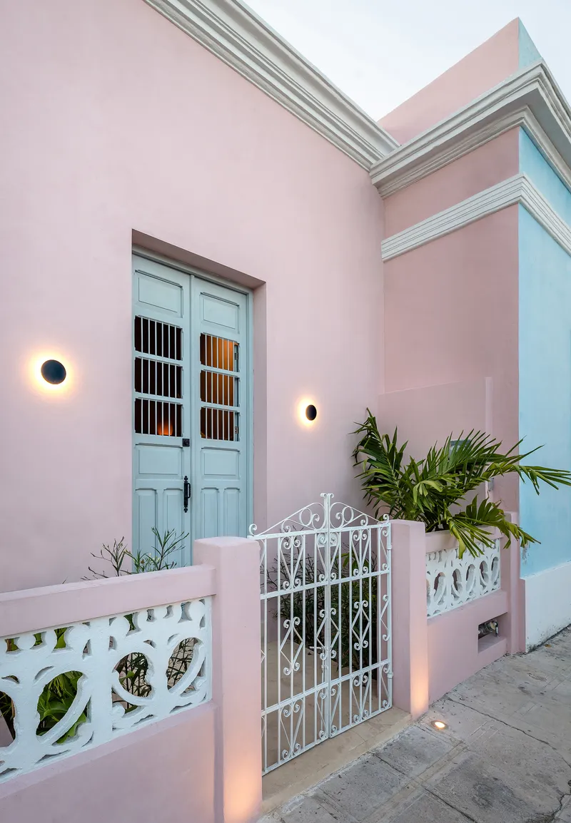 Entry gate with ornamental ironwork and pale blue doors flanked by wall sconces at dusk