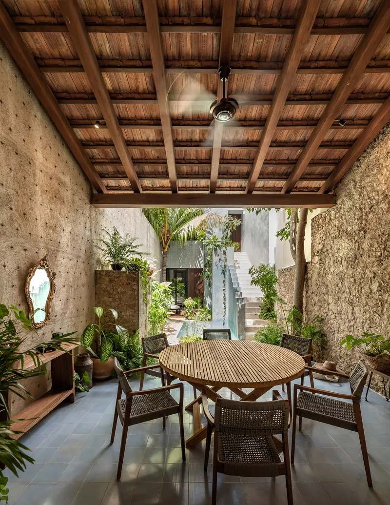 Covered dining area with timber ceiling, exposed beams, ceiling fan and view to planted courtyard beyond