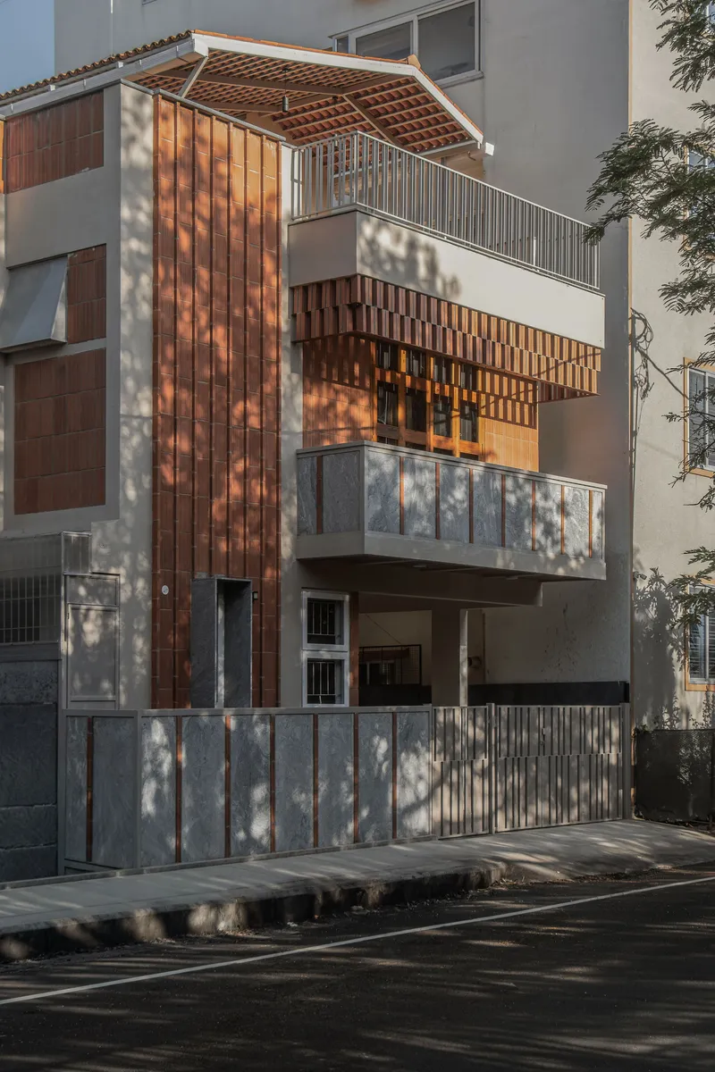 Street facade showing vertical timber slat screens and exposed terracotta roof tiles with tree shadows at dusk