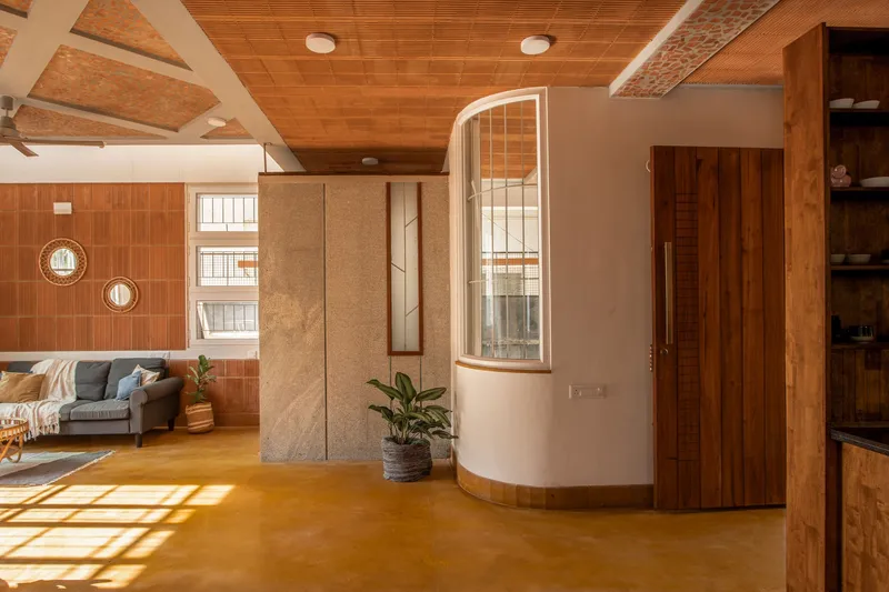 Living room interior with cork and timber ceiling, curved window bay, and sunlight streaming across the polished concrete floor