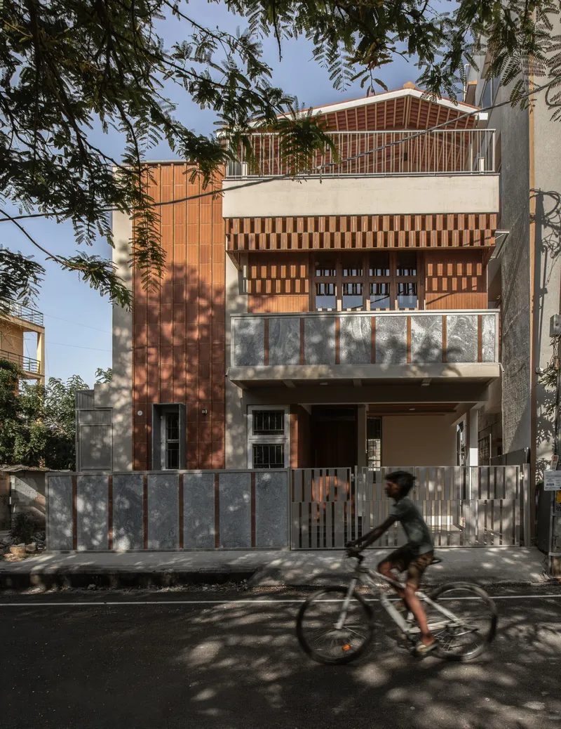 Street facade with vertical timber slats and chequered panels, framed by tree branches as a cyclist passes