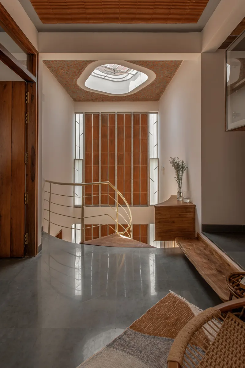 Spiral staircase with metal railing in double-height entry space beneath a geometric ceiling skylight