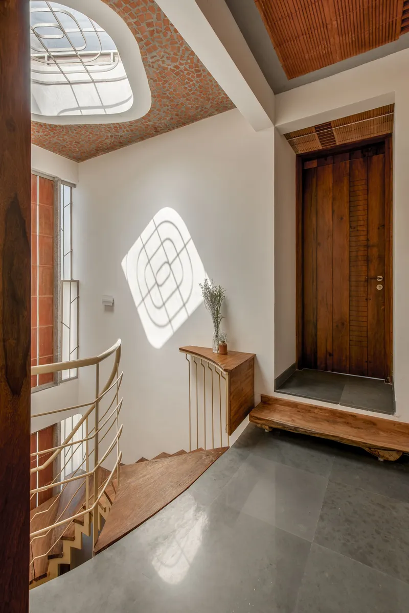 Entry hall with curved skylight casting geometric shadows onto a white wall above a timber door