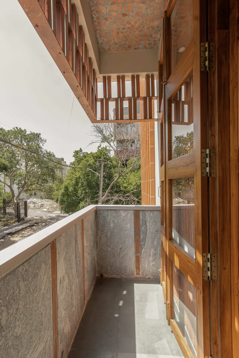Narrow balcony with stone panel walls and timber railings overlooking trees under an overcast sky