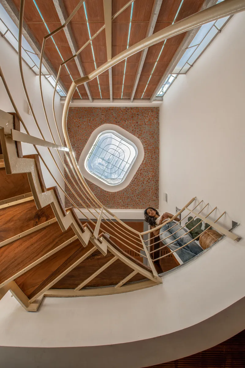 Top-down view of the spiraling timber staircase with rope railings and brick wall beneath a skylight