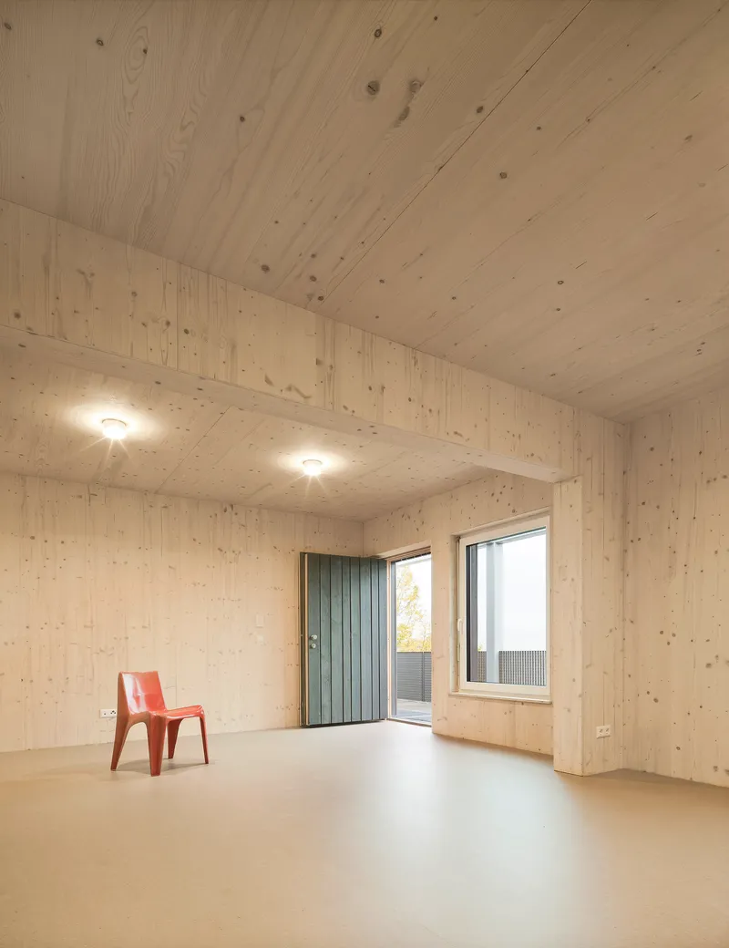 Interior room with light wood plank walls and ceiling, pale floor and a single orange chair near the window