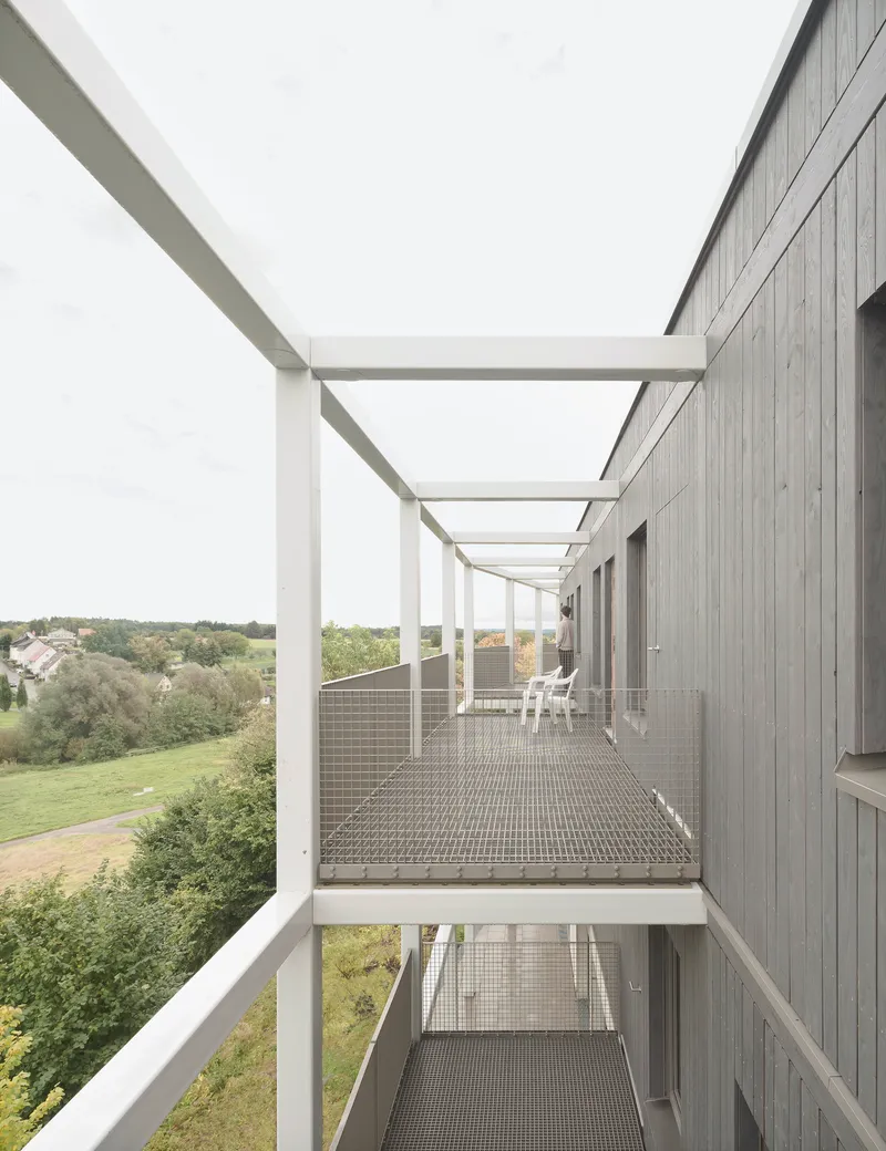 Exterior walkway with steel grating deck and white frame pergola overlooking a landscape of fields and trees