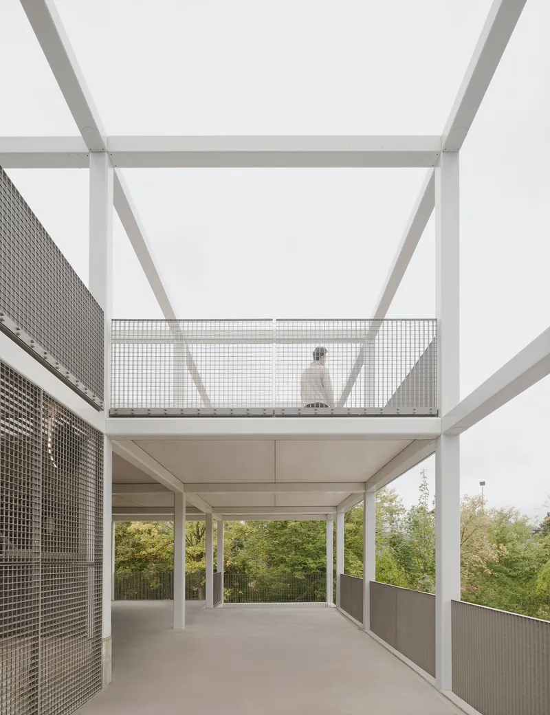 Open terrace with white steel structure and perforated metal balustrade with a figure walking on the upper level