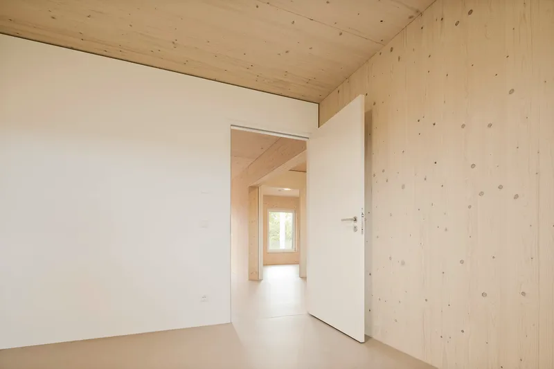 Doorway view through aligned rooms with exposed timber plank walls and white painted partitions under natural light
