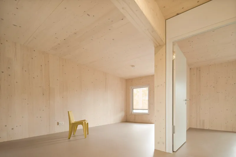 Interior room with light plywood walls and ceiling, pale resin flooring and a yellow plastic chair