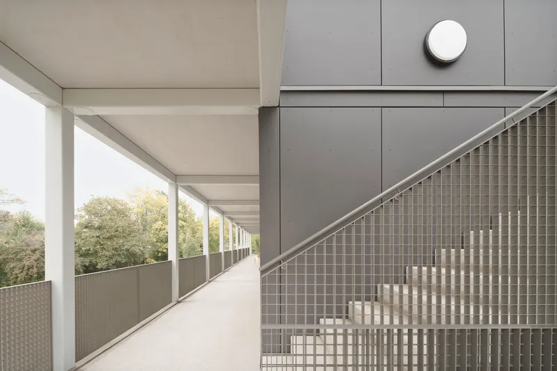 Exterior corridor with steel balustrade of woven metal mesh and gray panel cladding under overcast sky