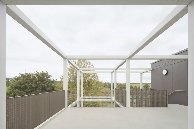 Open-air terrace with white structural frame, mesh balustrades and views to distant green countryside