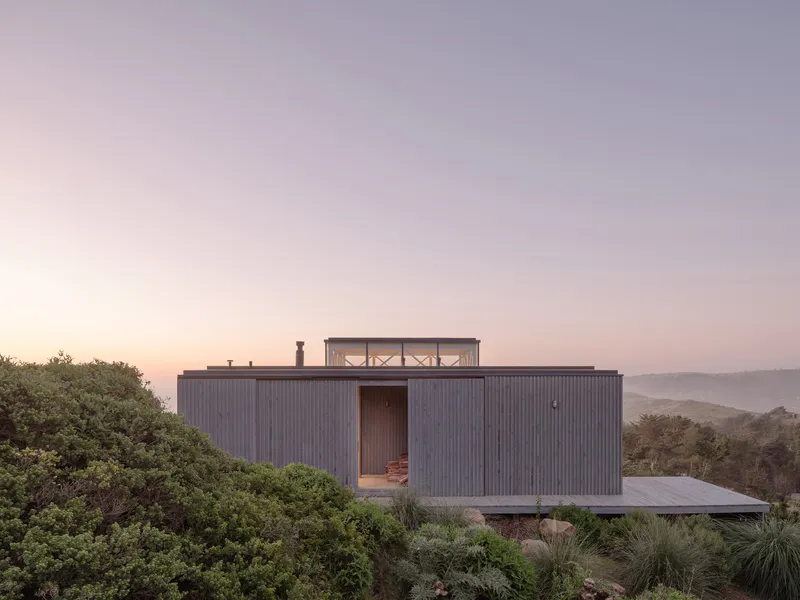 Vertically ribbed timber-clad volume with rooftop terrace overlooking coastal hills at dusk