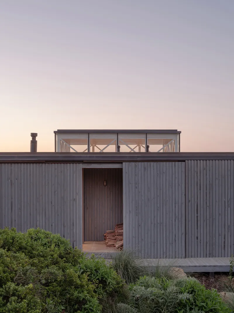 Corrugated metal facade with recessed entry and glazed roof pavilion above at twilight