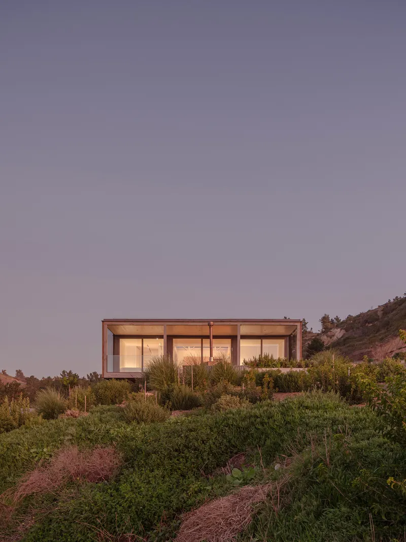 Glass facade with interior lighting nestled into hillside vegetation at dusk